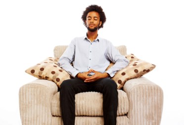 content young man sitting meditating in comfy chair on white